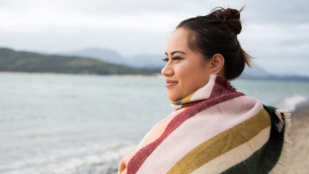 Woman standing on beach with blanket wrapped around shoulders