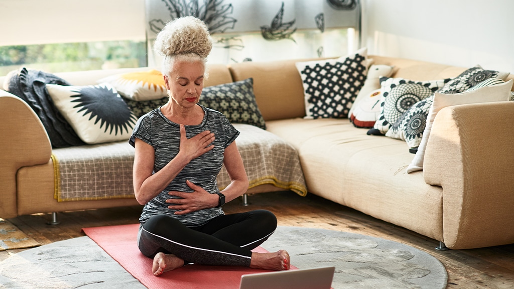 Senior woman with eyes closed meditating, sitting cross-legged on floor