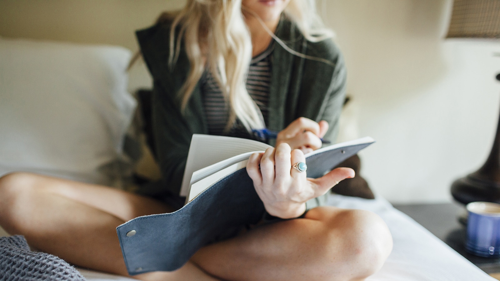Low section of woman writing diary while sitting on bed