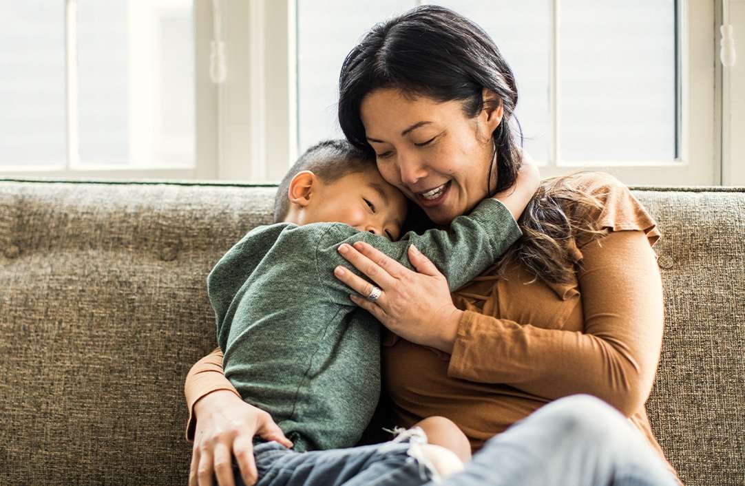 Mom and son sitting on brown couch hugging eachother