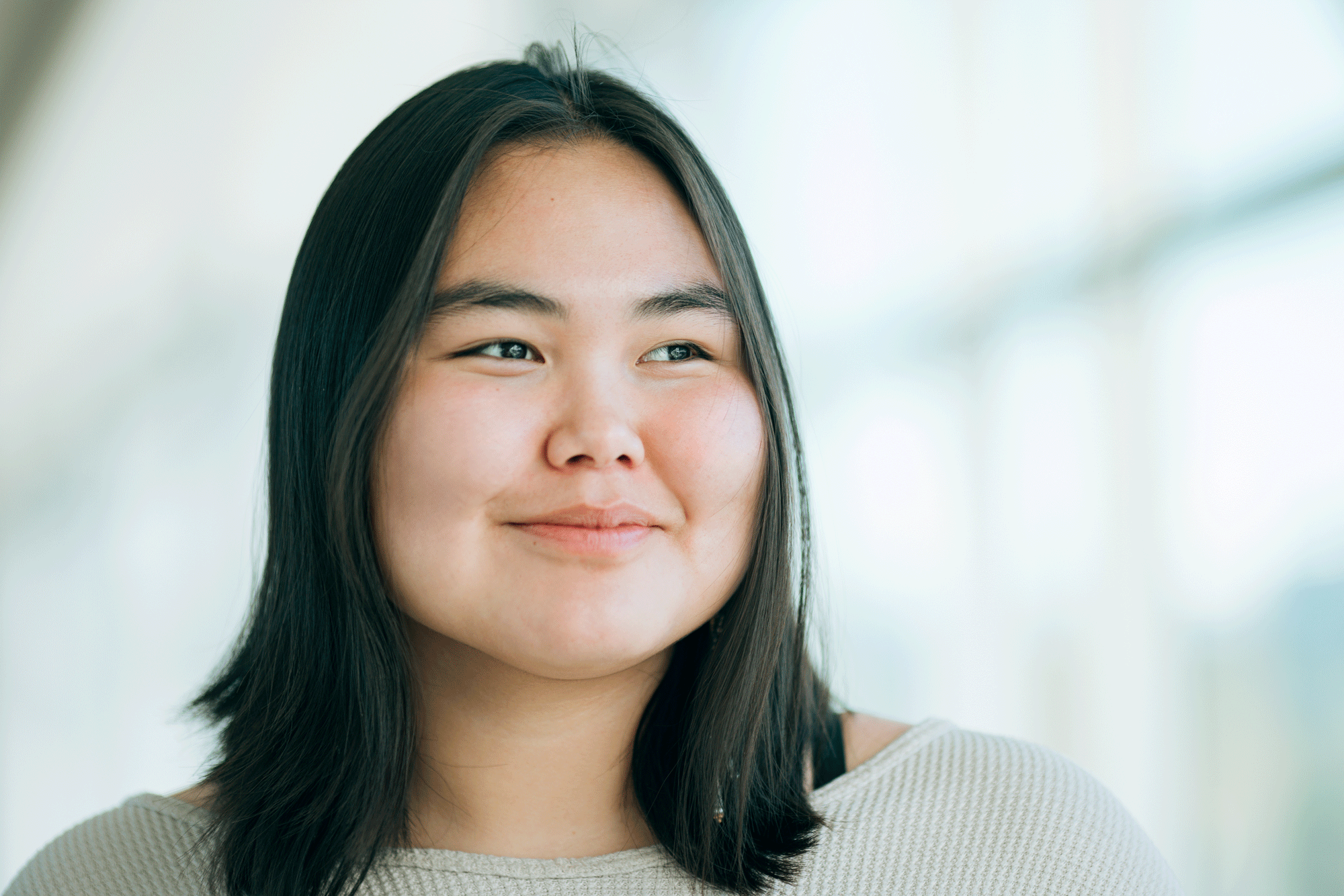 young woman standing in front of a bay of windows looking out with a slight smile